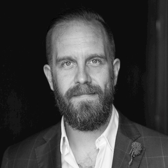 A person wearing a suit and tie smiling and looking at the camera

Description automatically generated